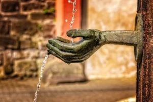 Bronze hand pours water over the edge of an outdoor fountain.